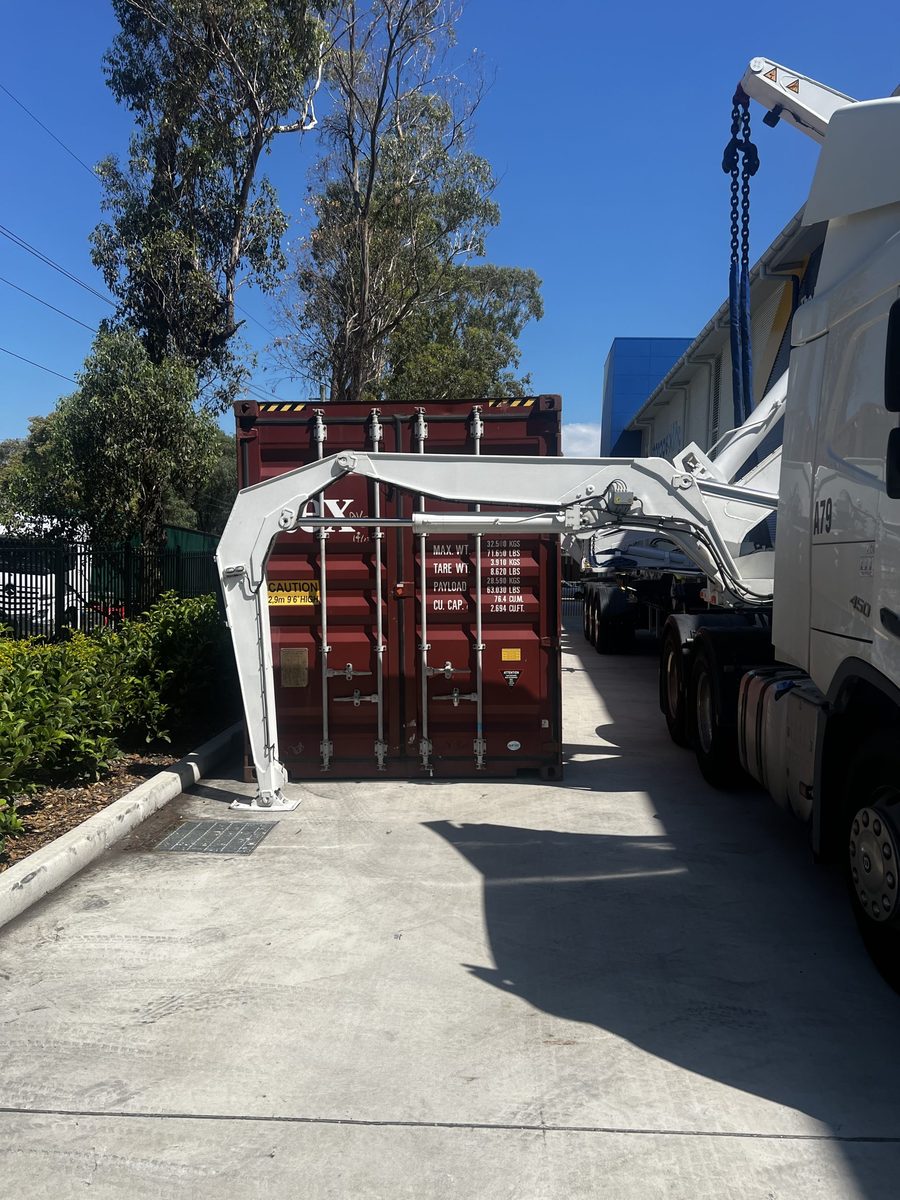 A side loader placing a shipping container on the ground in a narrow driveway